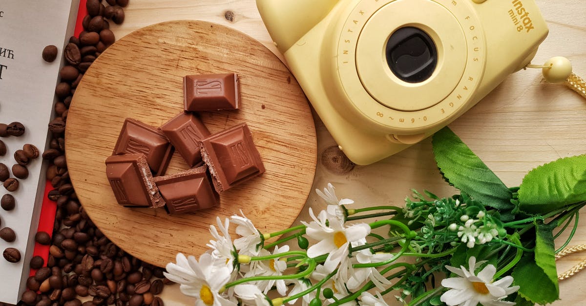 'Sweet milk' substitute in an old recipe - Top view of delicious pieces of milk chocolate bar with filling on wooden board near heap of aromatic coffee beans and instant camera with artificial chamomiles on table