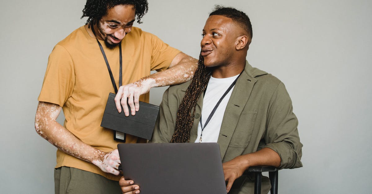 A different name for Manitoba flour? - Happy African American androgynous person with Afro braids and computer looking at black colleague with vitiligo and notebook while working on gray background