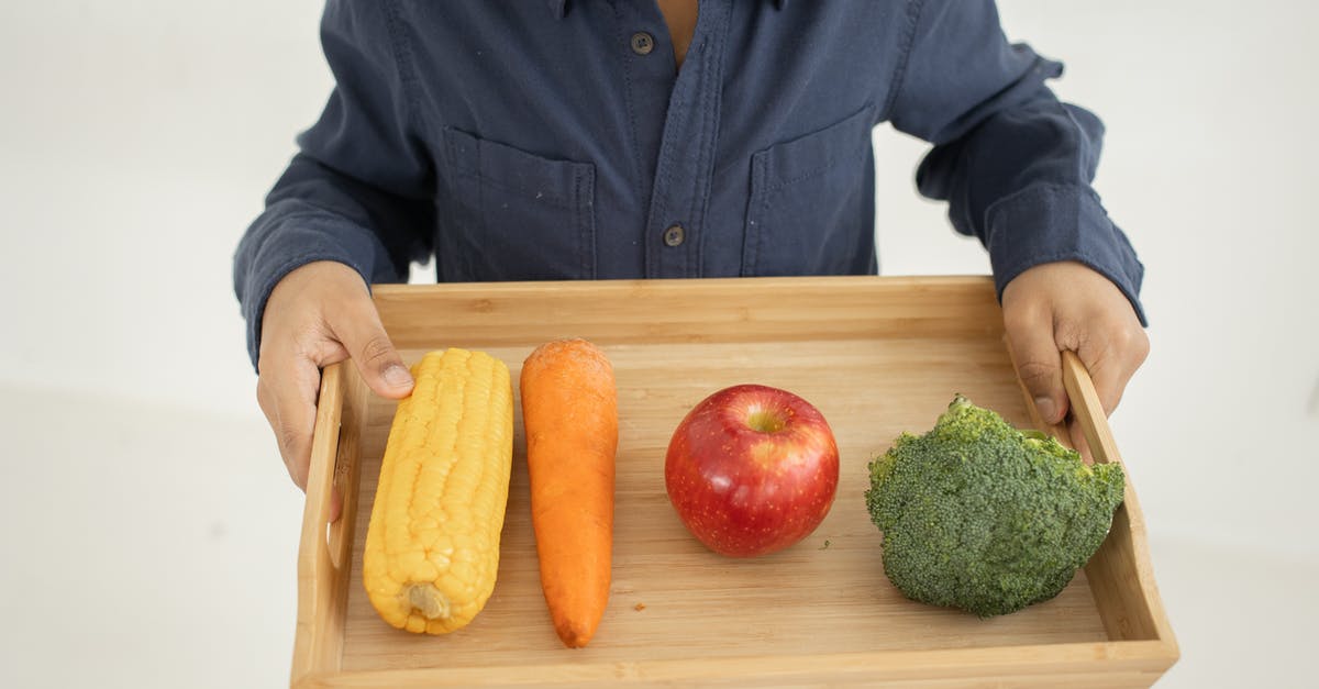 Accidentally ate raw corn starch, is it safe? - From above of crop anonymous kid in casual outfit holding wooden tray with fresh healthy broccoli apple carrot and corn against white background