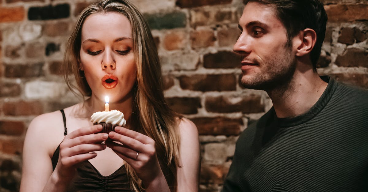 Accidentally beat sugar and butter together - Young couple in elegant outfits in restaurant while blowing in candle on small cupcake and celebrating birthday near brick wall