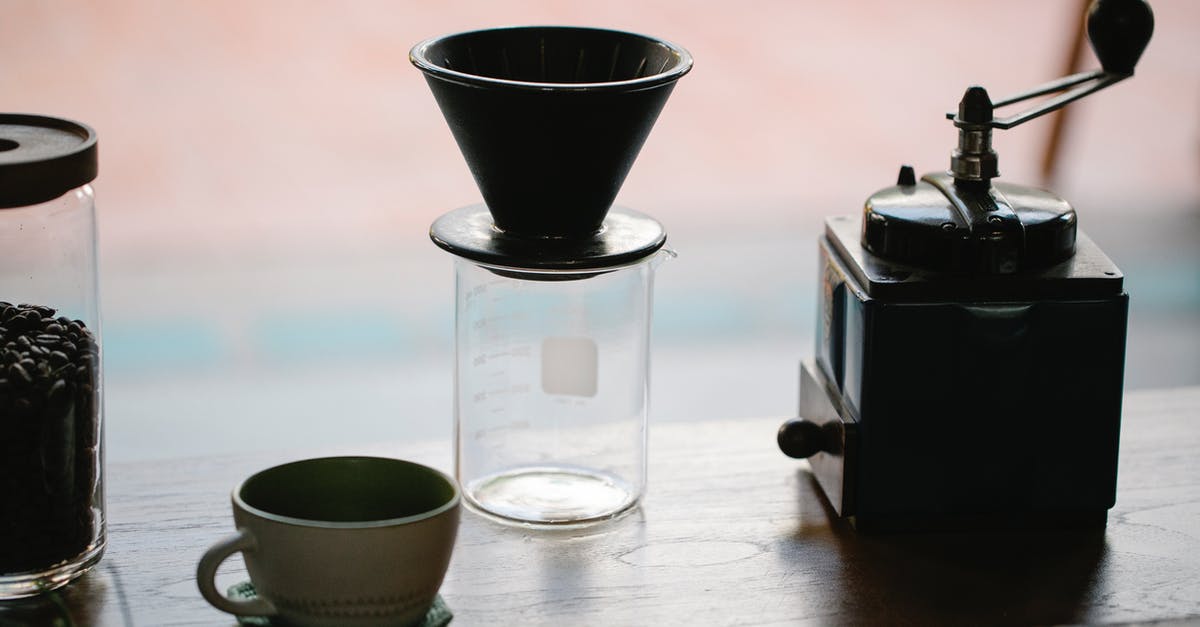 Achieving perfection via manual drip-brew coffee method - From above of manual coffee grinder with pour over coffeemaker placed in wooden table with ceramic cup and glass jug with roasted beans in morning