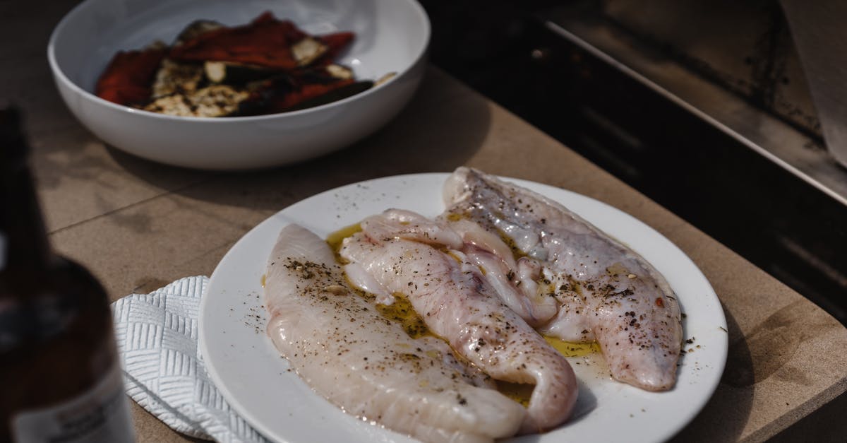 Add spice then oil, or oil then spice? - Tasty raw fish fillet covered with flavoring and oil served on plate near bowl with grilled vegetables on table with bottle of alcoholic drink