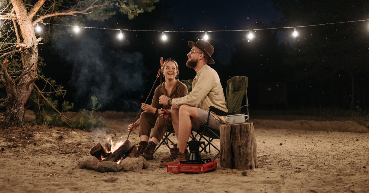 Adding 'netvet; to sausages - A Couple Sitting on Chair while Grilling on Campfire