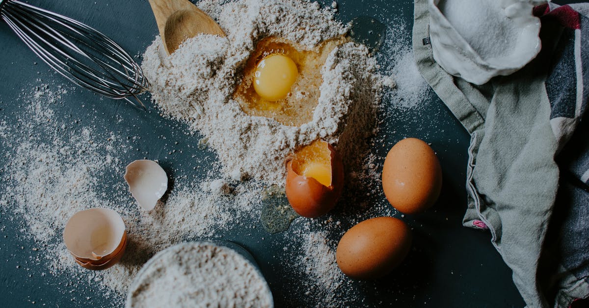 Adding butter to pizza recipe - From above of broken eggs on flour pile scattered on table near salt sack and kitchenware