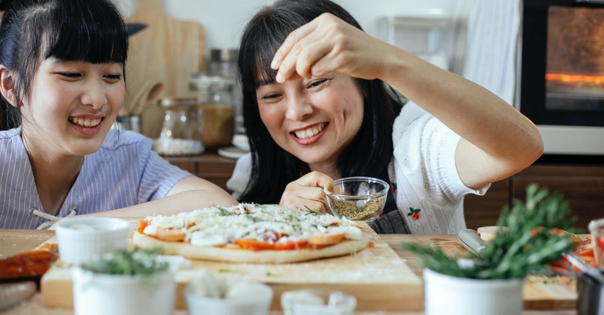 Adding butter to pizza recipe - Cheerful Asian women sprinkling seasoning on pizza