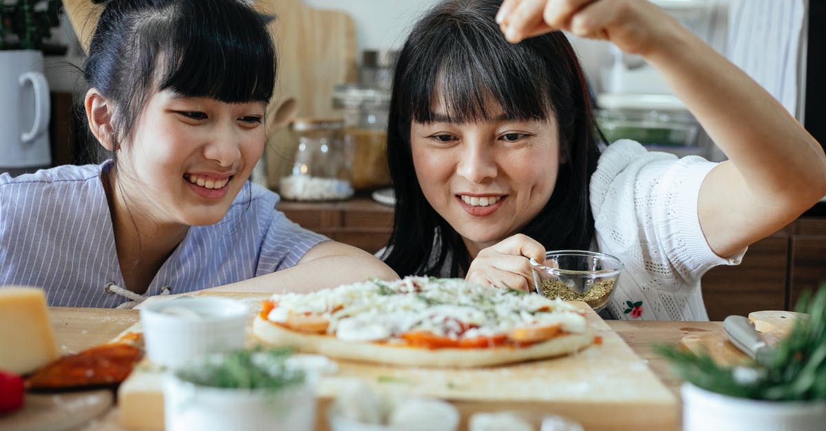 Adding butter to pizza recipe - Cheerful ethnic women seasoning pizza with spices