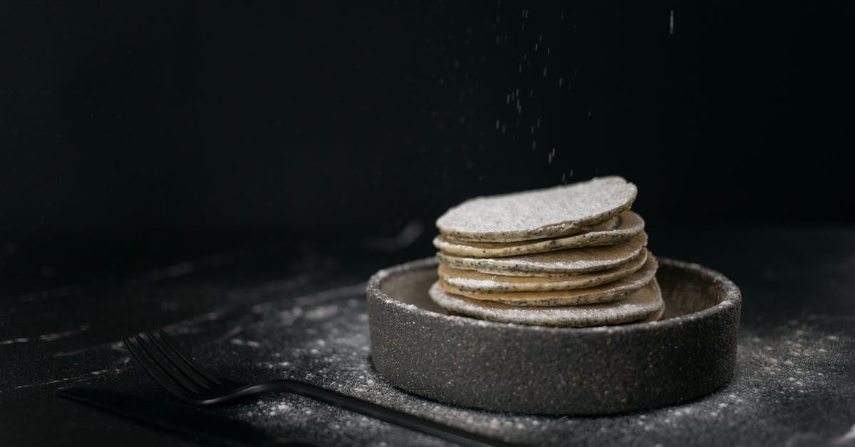 Adding chili powder to a dish makes it dark black - Delicious sweet pancakes placed in baking dish near metal fork and knife on table on black background