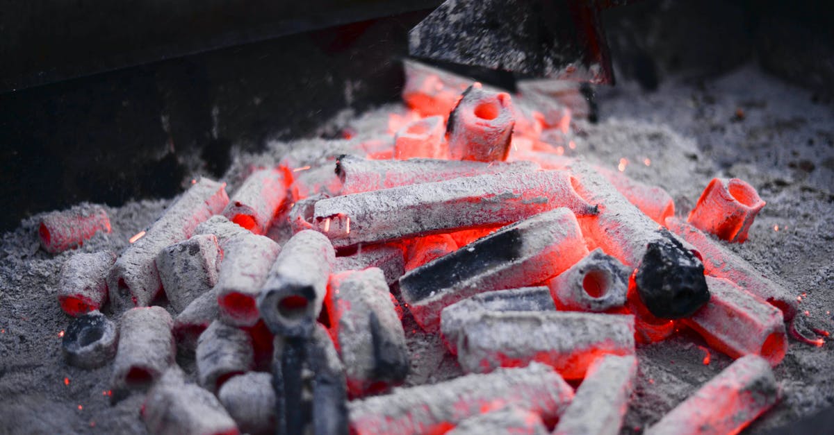 Adding fuel to a grill during long cooking - Small hexagonal coals with holes smoldering on metal rack before roasting barbecue in nature