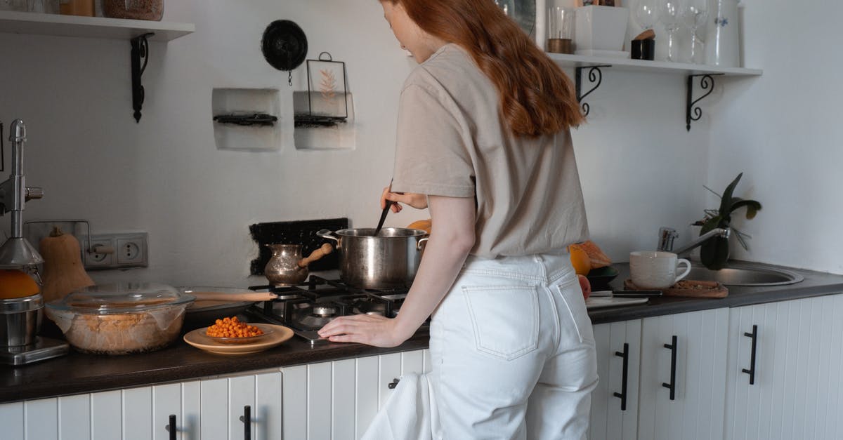 Adding liquid to Le Creuset Casserole during cooking - Woman in Brown Shirt and White Pants Standing in Front of Stove