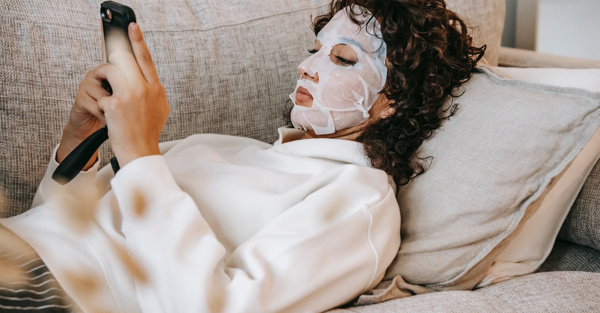 Adding moisture to gluten free muffins - Side view of female wearing facial moisturizing mask surfing cellphone while lying on couch in living room during skincare routine