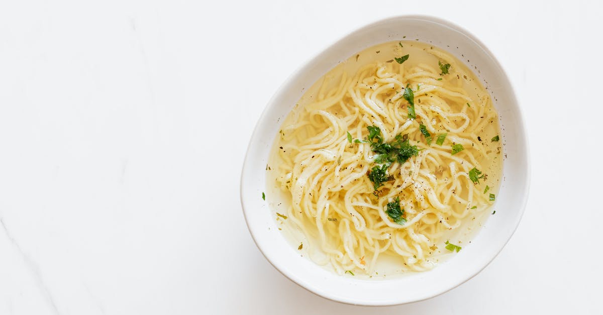 Adding parsley at the beginning of making chicken stock - Top view of white bowl with yummy homemade noodles cooked in fresh delicious chicken broth and topped with green aromatic parsley placed on white marble table