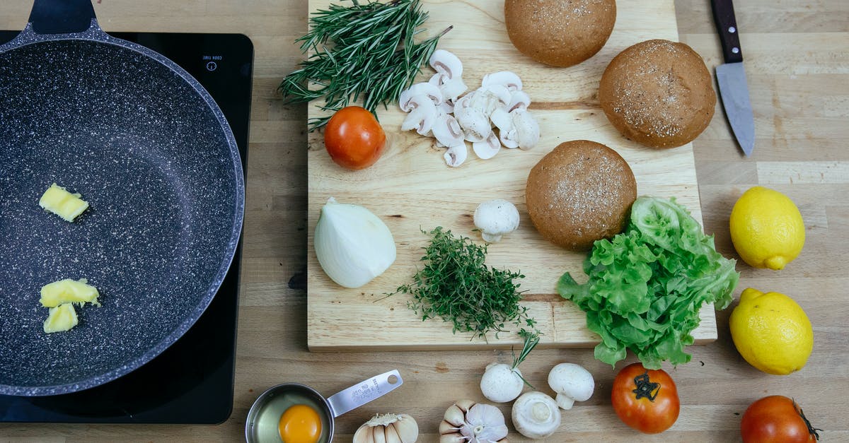 adding peanut butter to a recipe - Top view of pan with butter on stove placed near wooden board with buns greens and fresh vegetables in kitchen