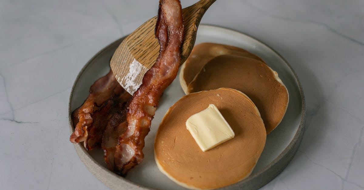 adding peanut butter to a recipe - High angle of delicious pancakes with butter piece near sliced fried bacon and wooden kitchen spatula on plate on white table in bright place