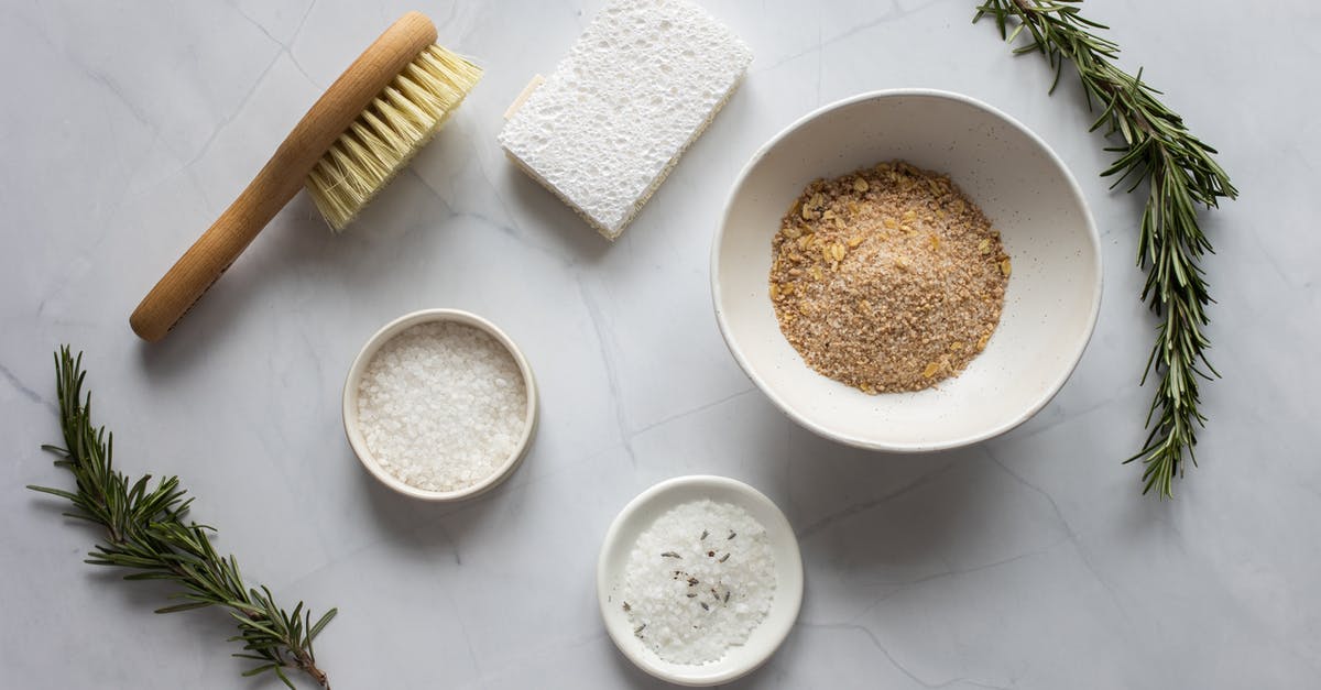 Adding Pure Oleogustus Flavor - Top view of bowls with ingredients for organic scrub arranged with pumice stone and fresh branches of rosemary