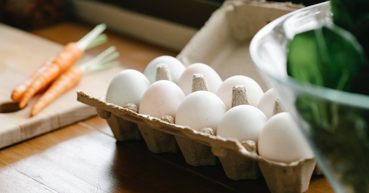 Adding raw chicken to a meal that is being reheated - Carton box with white organic eggs placed on kitchen counter near chopping board with carrots