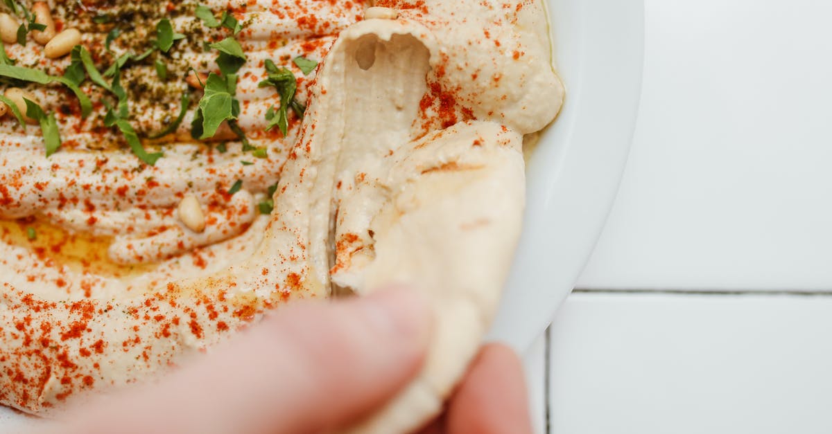 Adding rolled-in seasonings to pita bread - Close-Up Shot of a Person Holding a Humnus Bread