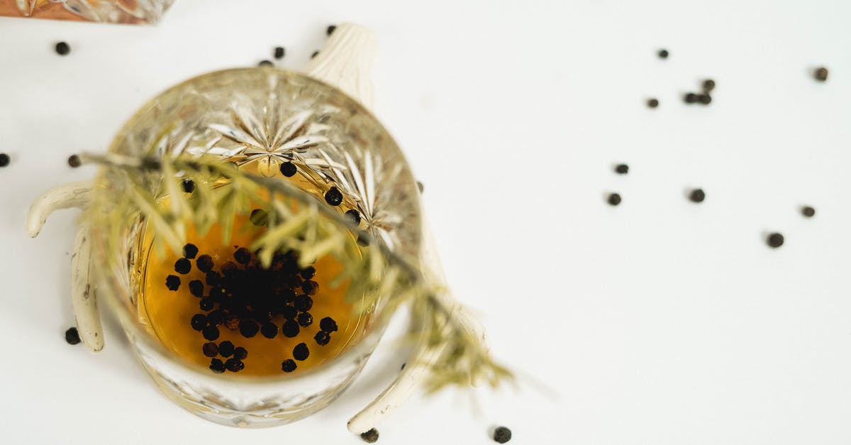 Adding spice to poaching liquid - From above glass of whiskey with black peppercorns decorated with green rosemary twig placed on white background in light room