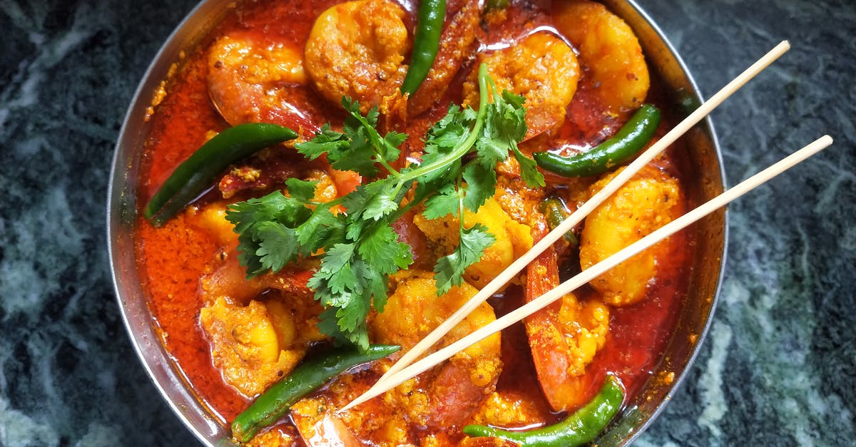 Adding spiciness to indian curry at the end of cooking - Shrimps in Sause with Green Chili Peppers and Parsley in Round Dish with Chopsticks