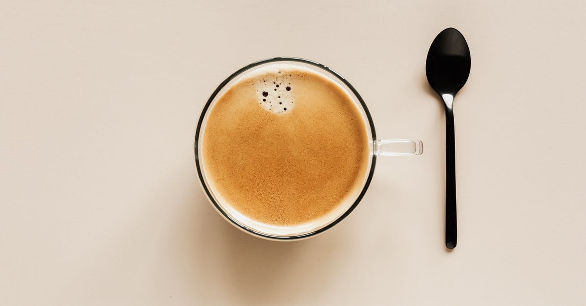 adjust flavor from inexpensive brandy - From above of clear glass cup with hot aromatic drink placed near black metal spoon on beige table for coffee break