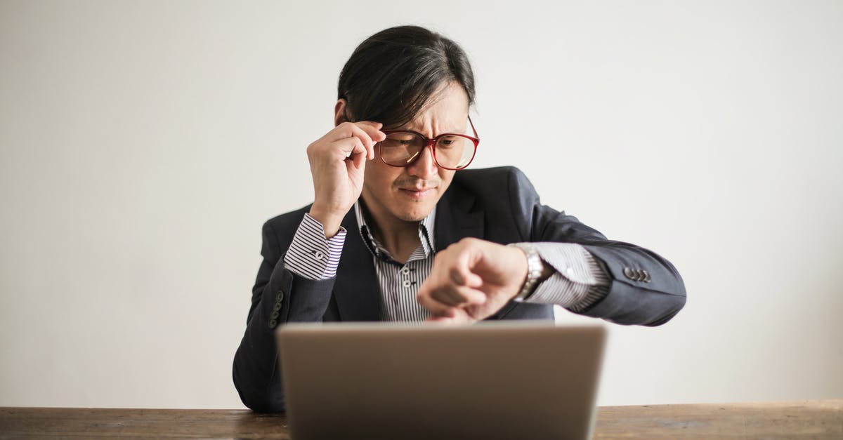 Adjusting pressure setting and processing time when modifying pressure canning recipe - Young frowning man in suit and glasses looking at wristwatch while waiting for appointment sitting at desk with laptop