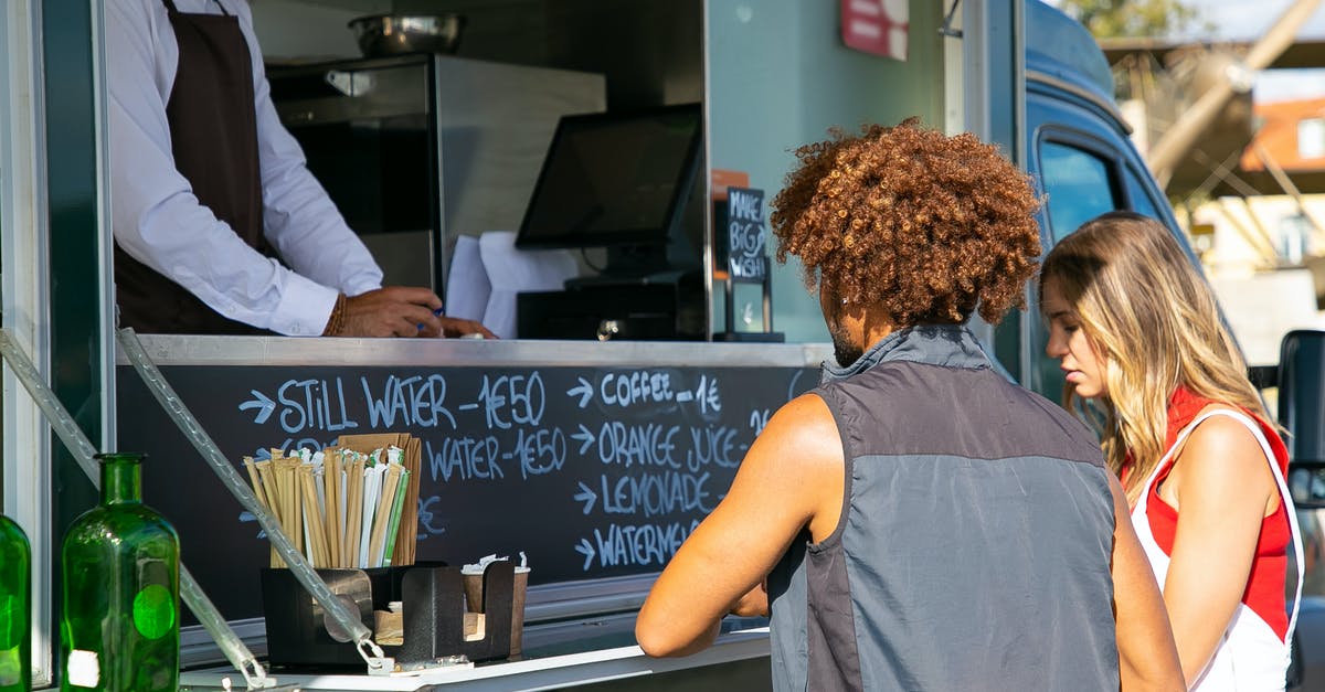 Advice on bulk buying nuts - Multiethnic couple standing together near food truck with seller and selecting dishes from menu in sunny day