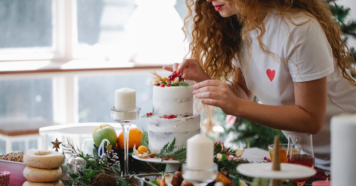 Advice on two-tier cake and height - Crop serious female adding berries on top of two tier cake for festive dinner for New Year holiday