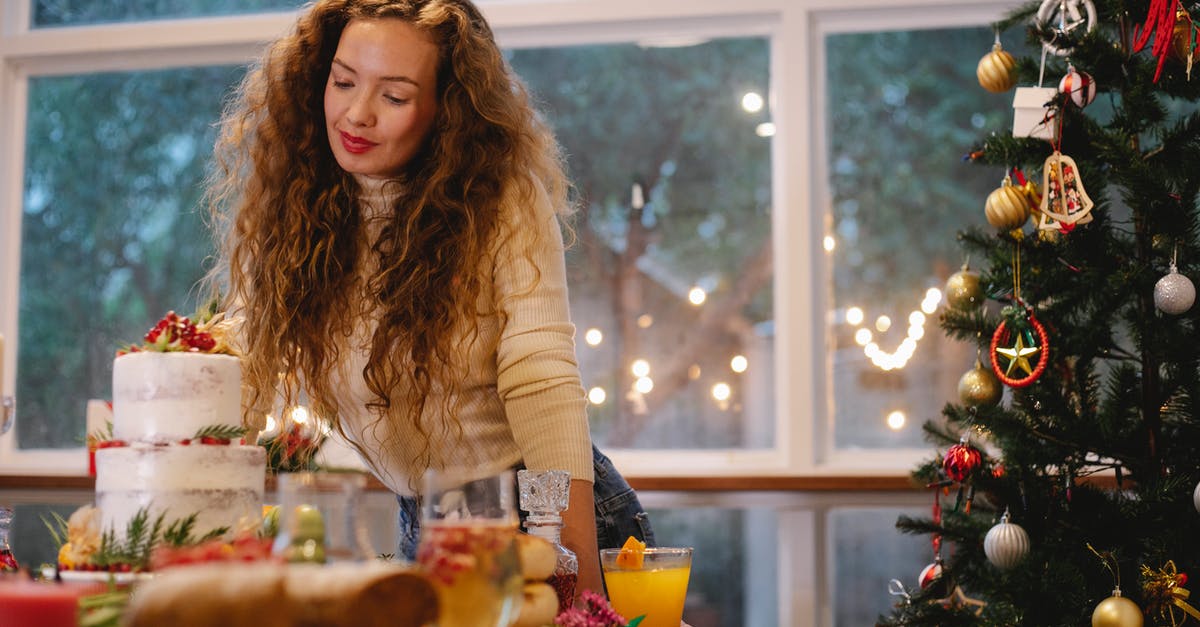 Advice on two-tier cake and height - Low angle of serious female leaning on served festive table with two tier cake near decorated Christmas tree