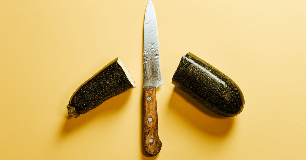 Age between mild and sharp - From above of fresh sliced zucchini placed on yellow background with sharp knife with wooden handle between halves of vegetable