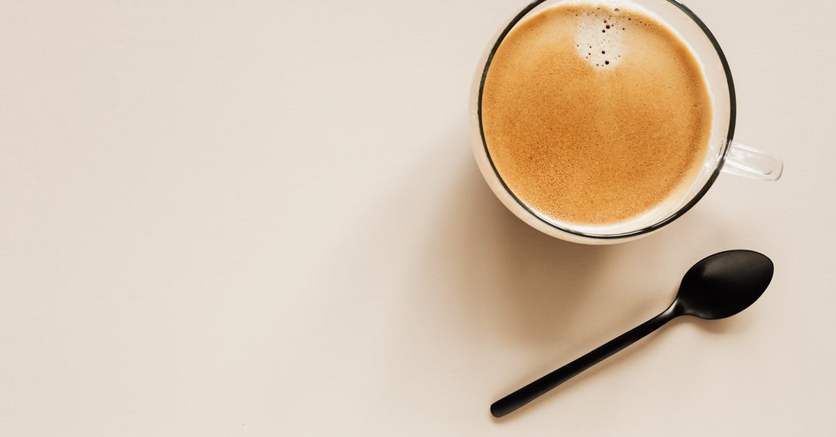 Air bubble on surface of chocolate - Top view of glass of aromatic light brown coffee with foam and small bubbles on top near metal spoon on beige surface