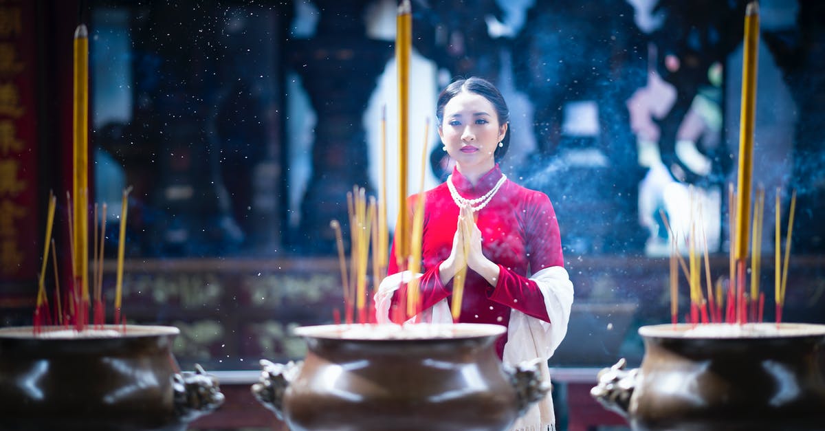 All Clad Copper Core - everything sticks, why? - Calm young Asian woman with dark hair in elegant red dress praying with clasped hands while standing near copper pots with burning incense sticks in Buddhist temple