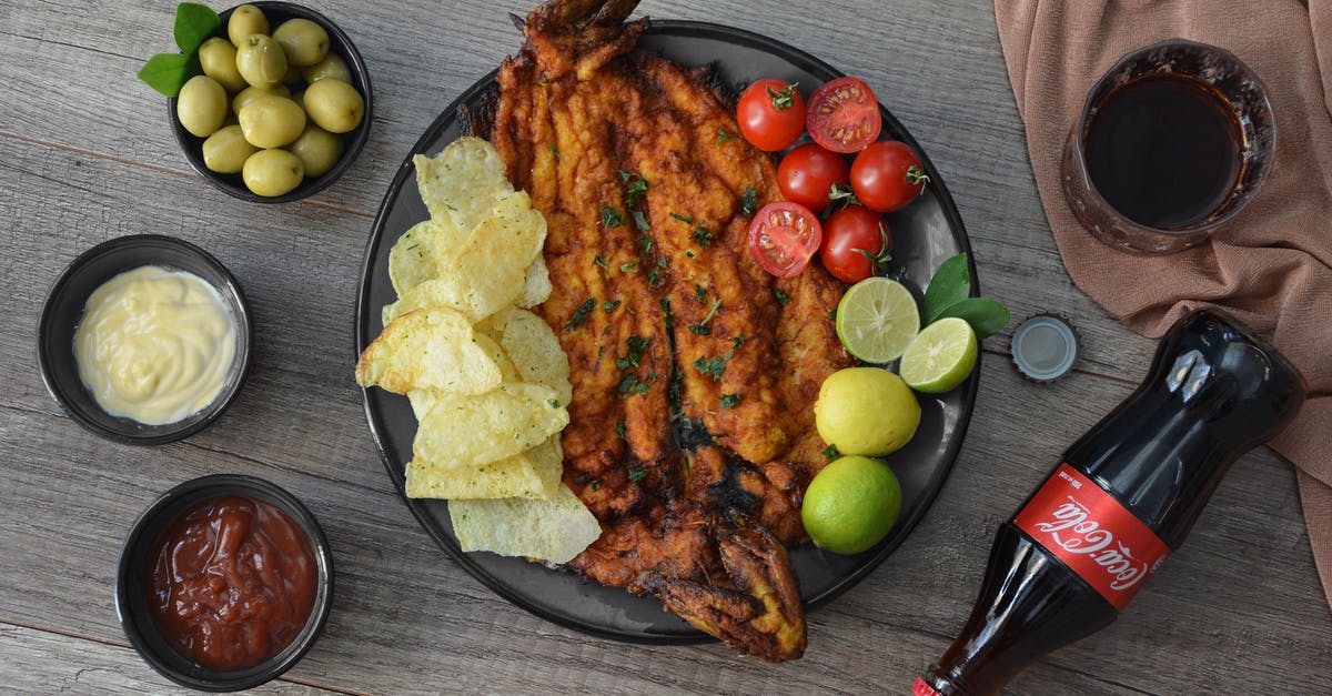 Alternative fish for Fish and Chips - Top view of appetizing fried fish garnished with crunchy potato chips with limes and cherry tomatoes near ketchup and glass of refreshing drink