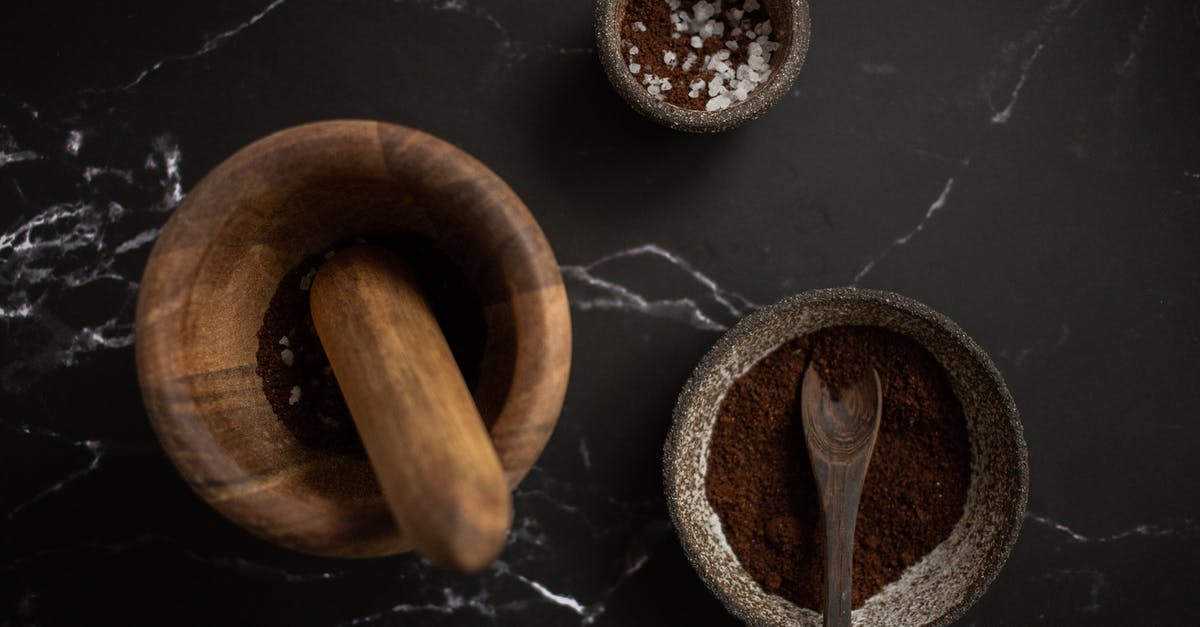Alternative to salt when using Mortar and Pestle - High angle of wooden mortar and pestle placed near ceramic bowl with aromatic coffee on black marble table
