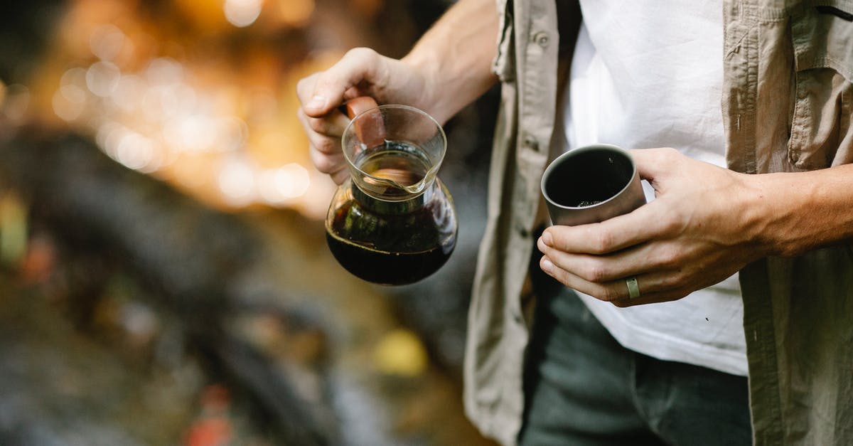 Alternatives to coffee - Crop anonymous male camper pouring freshly brewed coffee from chemex coffeemaker into metal mug while resting in autumn forest during trekking