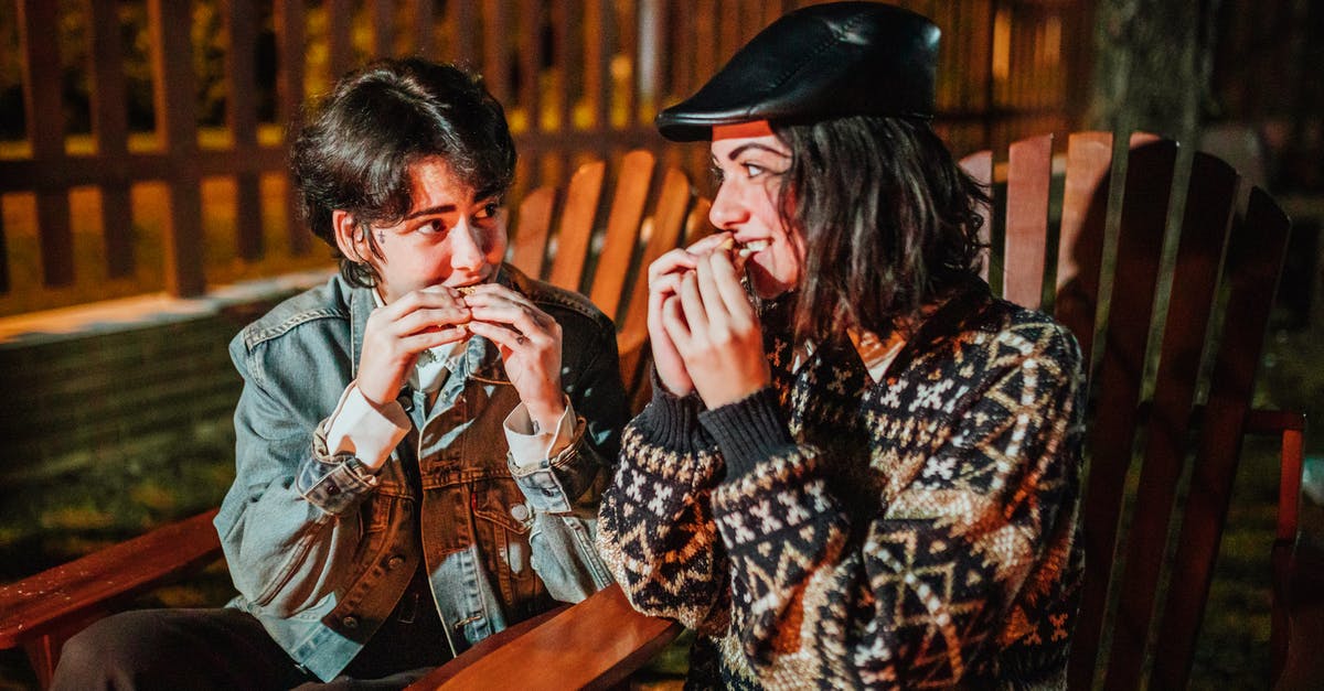 American equivalent for British chocolate terms - Smiling female friends looking at each other while eating tasty campfire treats in armchairs against fence in evening