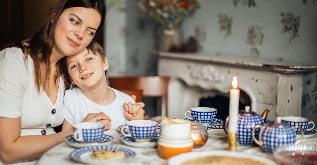 Anise Cookies: Why 12-hour rest before baking? - Cheerful woman cuddling son while sitting in cozy kitchen with candle and blue tea set having crepes and cookies for meal