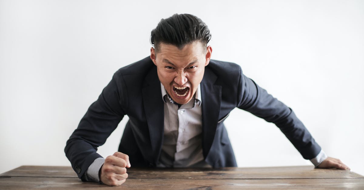 Another crockpot error - Expressive angry businessman in formal suit looking at camera and screaming with madness while hitting desk with fist