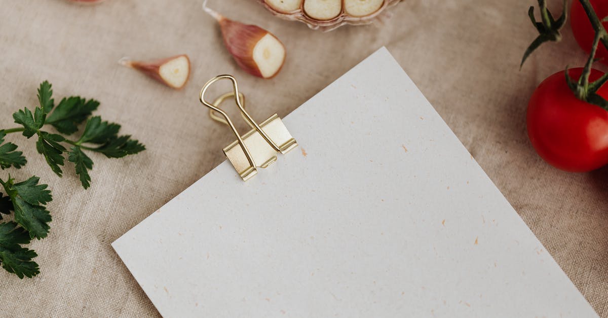 Are cardamom husks edible? - Top view of empty sheet of paper fixed with metal clip and placed near garlic gloves and ripe tomatoes with parsley on linen towel