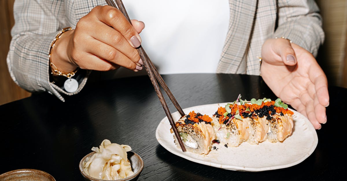 Are egg rolls supposed to be eaten with chopsticks or hands? - Hands of a Wooden Using Chopsticks on Sushi Rolls