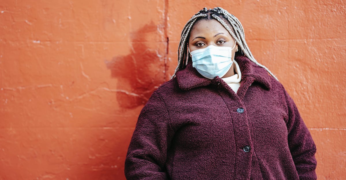 Are purple spots in freezer safe? - Pensive African American female with dreadlocks in casual clothes and protective mask standing near red painted wall on street and looking at camera