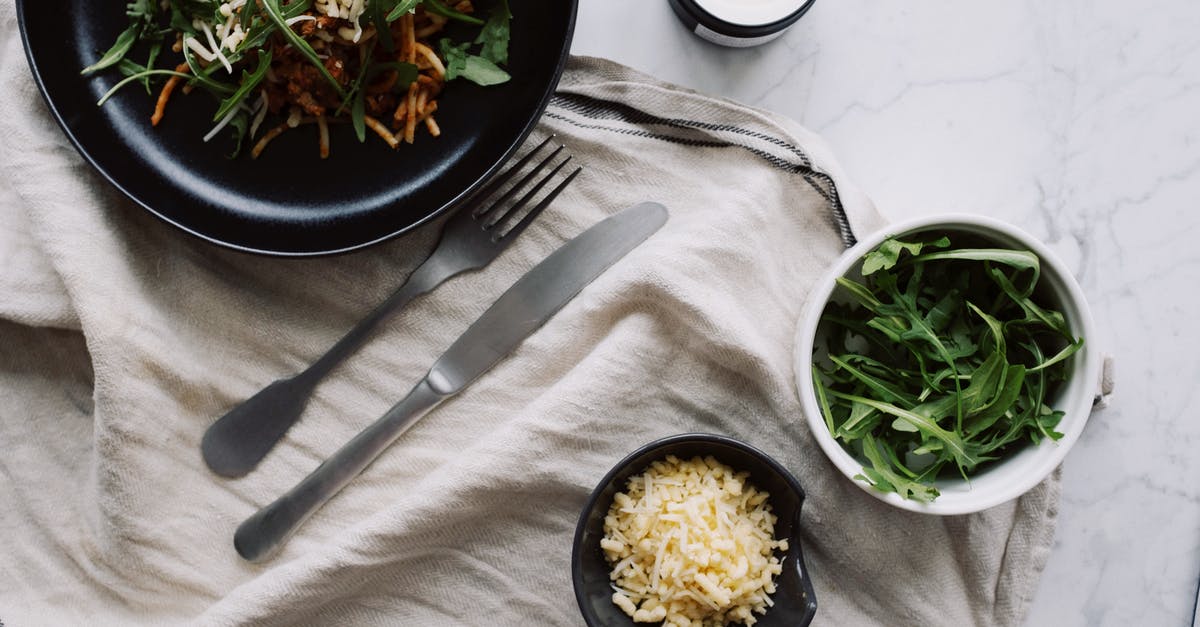 Are the white crystals on my American Cheese safe to eat? - Top view of tasty vegetable salad served on black plate with fork and knife placed on white napkin near candle and cup with herb