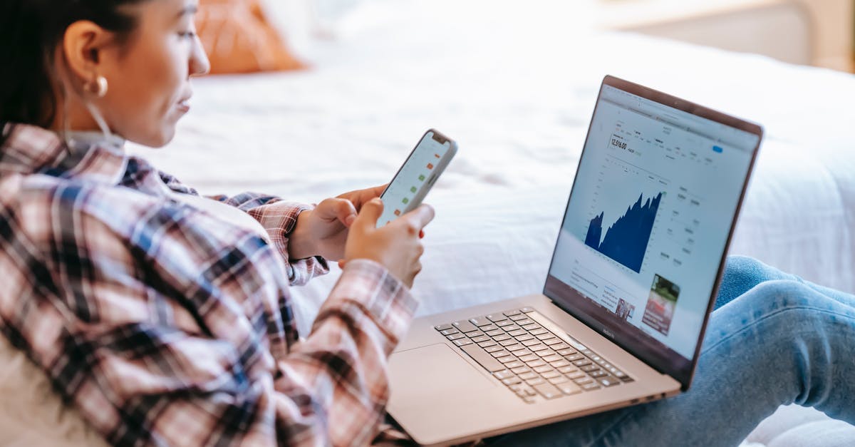 Are there any benefits in refrigerating stock before using it? - Side view of crop ethnic female dealer using trading app on cellphone against netbook with graph on screen in house