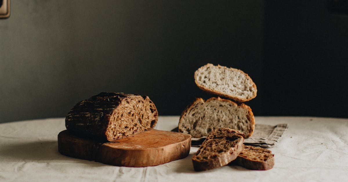 Artisan sourdough bread - Slices of tasty freshly baked sourdough bread placed on crumpled tablecloth on table with cutting board in light room on black background