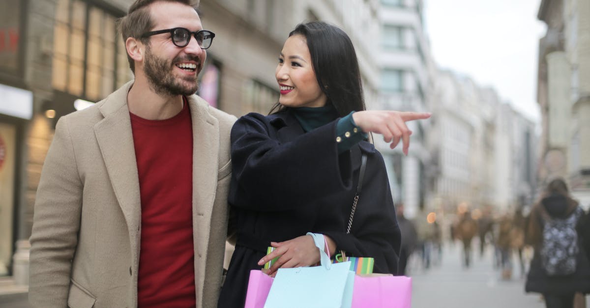 At what point should carrots be thrown away? - From below happy stylish Asian woman in warm clothes smiling at cheerful unshaven man in glasses and pointing finger away while walking along street together in city after shopping