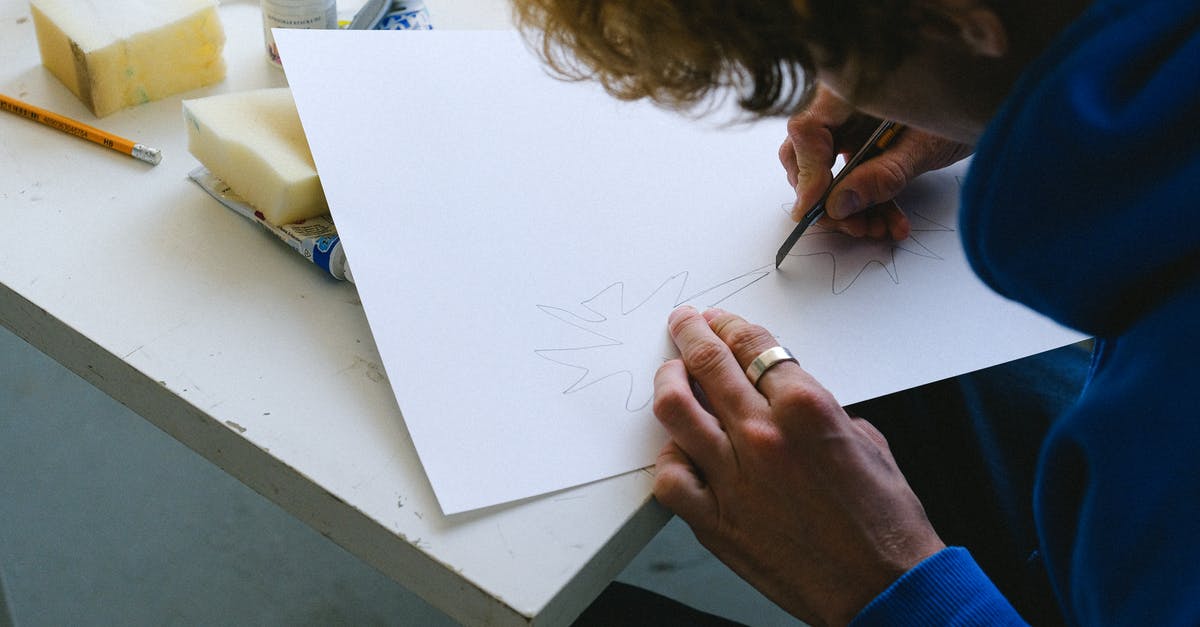 Bagel Sponge: Room Temp or Proofing Temp? - High angle of crop unrecognizable man in casual clothes sitting at table while cutting sketch on paper with utility knife near paints and sponge with pencil in light workshop