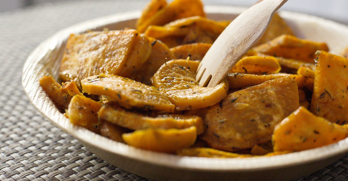 Baked sweet potato skin hard as a rock - Closeup of bowl full of crispy baked sweet potatoes with herbs and eco friendly bamboo fork