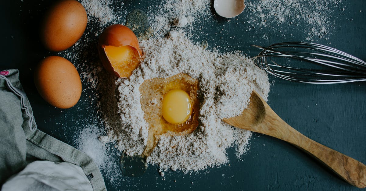 Baking and a rotten egg was cracked into mix :( - Top view pile of flour on table with broken egg arranged with wooden spoon and metal corolla during preparation of homemade dough