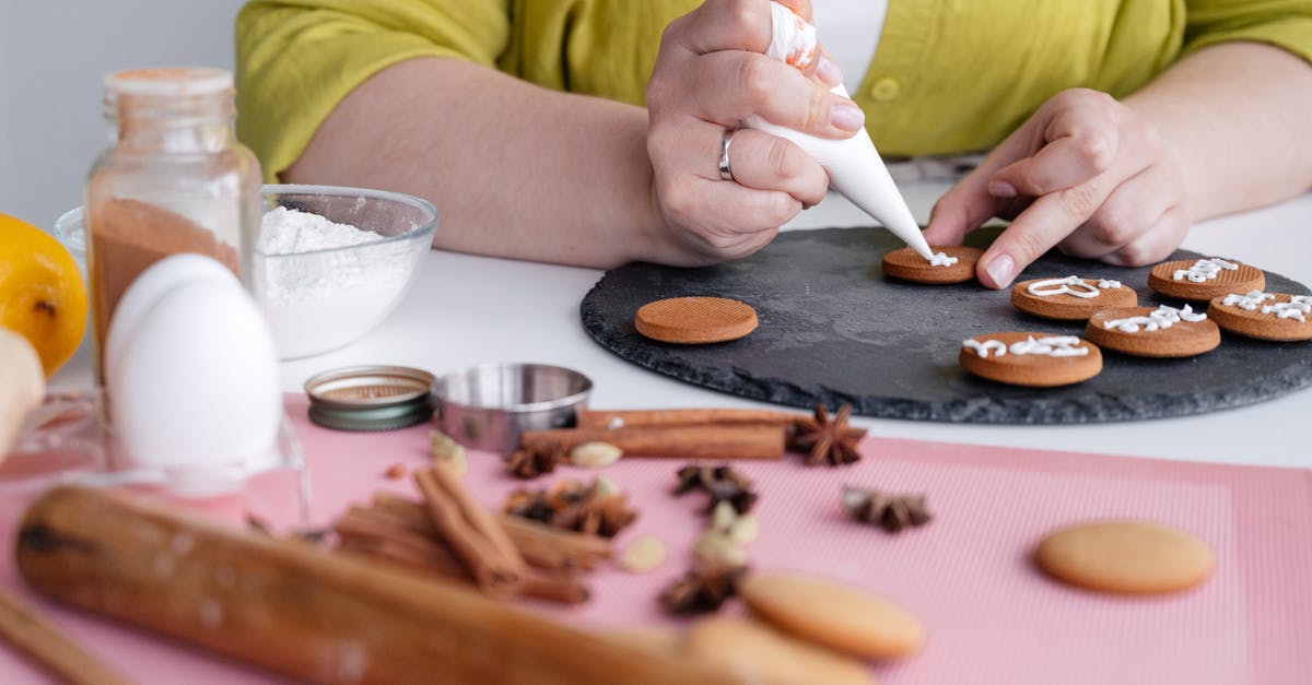 Baking flour and sour cream -US /UK terms [duplicate] - Crop anonymous female confectioner decorating delicious homemade cinnamon cookies with icing sitting at table near flour and cinnamon sticks