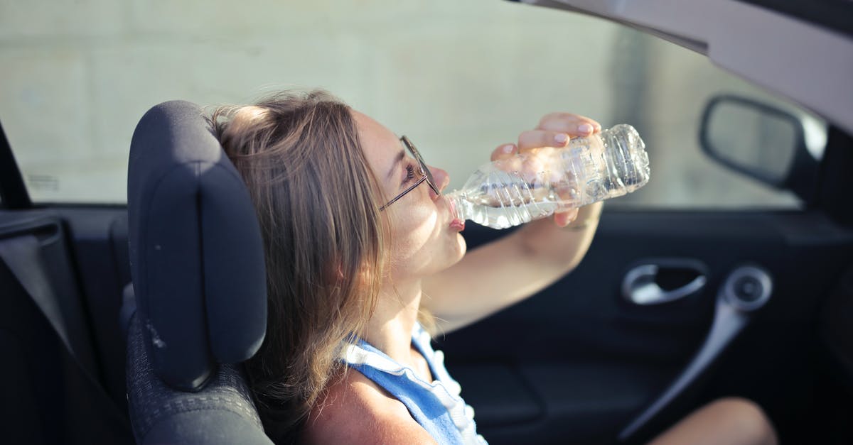 Baking in drinking glasses -- heat vs. logo paint, other issues - High angle side view of young woman in glasses and casual clothes drinking water from plastic transparent bottle while sitting in cabriolet with open roof in traffic jam in hot sunny day