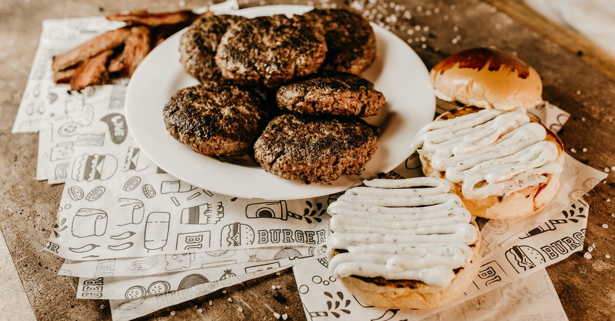 Baking with unhulled sesame seeds versus hulled - From above of bacon near plate with roasted appetizing patties for burgers and yummy golden bun on ornamental paper sheets on wooden table with sesame seeds