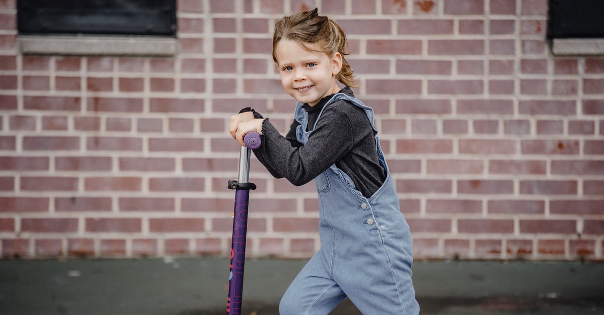 Balance overly sweet liqueurs - Side view of happy little girl in denim outfit smiling while riding scooter and looking at camera